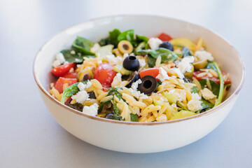  healthy orzo salad served in a bowl, made with fresh vegetables, black olives, and crumbled feta cheese close up