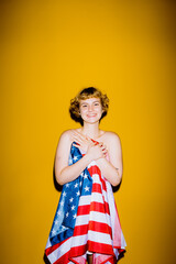 A cheerful young person holds an American flag wrap with a glowing yellow background. Their bright...