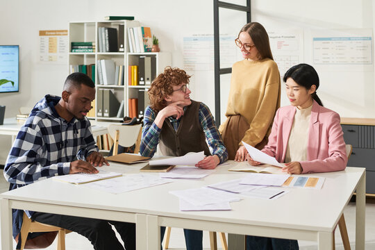 Multiracial group of students engaging in studying foreign languages in classroom with various study materials and discussion happening among participants