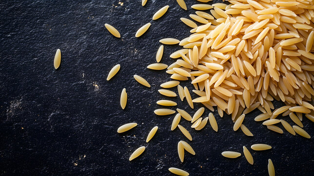A pile of orzo pasta grains scattered across a dark surface, resembling rice, with a subtle sheen reflecting off the pasta.