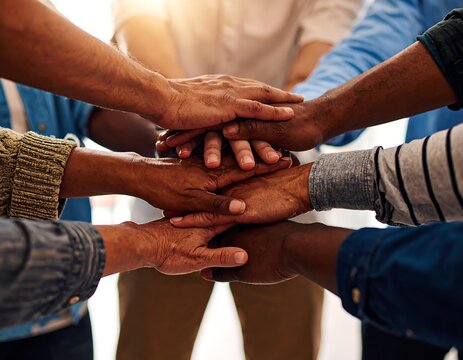 Group of diverse people stacking their hands together in a show of unity and teamwork outdoors.