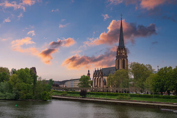 The Frankfurt Cathedral's Gothic spire rises near the Main River, surrounded by greenery, a...