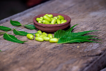 Fresh Neem fruit on wooden bowl and neem green leaf on rustic wooden background.