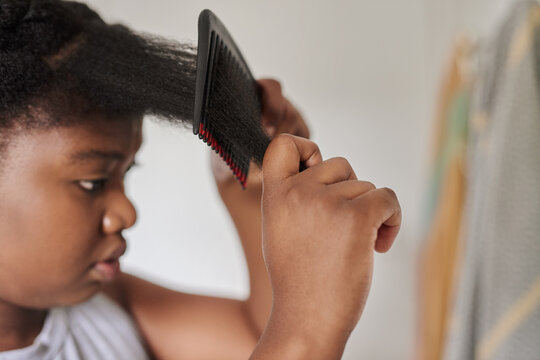 Young African woman combing her hair with a pic in the morning