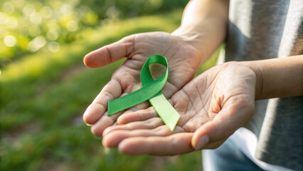 Hands holding green awareness ribbon outdoors in natural light  