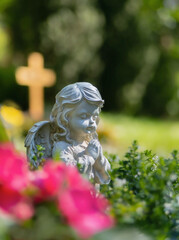 Kleiner Engel sitzt betend in Blumen, vor Holzkreuz