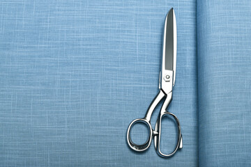 Top down view of lightweight linen fabric with professional sewing scissors resting atop. The soft,...