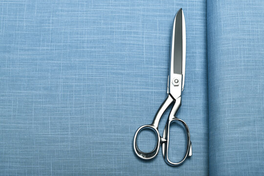 Top down view of lightweight linen fabric with professional sewing scissors resting atop. The soft, natural texture embodies craftsmanship, tailoring, and timeless textile artistry.