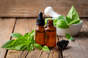 Basil essential oil and fresh leaves on wooden table, closeup