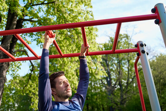 Male athlete training on red monkey bars in outdoor gym. Man doing sport exercises in open air park for wellness and body control. Concept of fitness, endurance and healthy lifestyle - Powered by Adobe