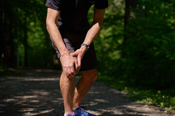 Runner holding knee in pain during workout in summer park. Man has injury while running. Male...