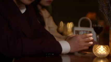 Couple sitting apart at a bar, avoiding eye contact, tension visible in their body language