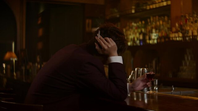 Lonely man sitting at bar with a drink, cigarette in hand, reflecting a sad mood