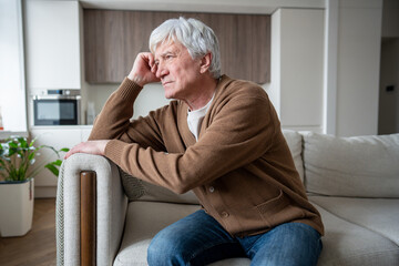 Aging senior man sits alone in empty living room staring vacantly, struggling with memory loss....