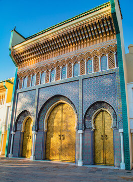 Magnificent golden gate of the Royal Palace of Fez, adorned with colorful traditional Moroccan mosaics under a bright blue sky.