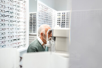 Senior man testing eyesight and diopter in ophthalmology clinic. Eyeglasses in background.