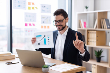 Young adult male business professional presenting charts and financial data in office. Confident...