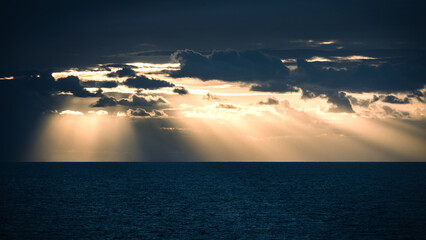 Beautiful sunset over the ocean with rays of sunlight piercing through dark clouds in the evening sky