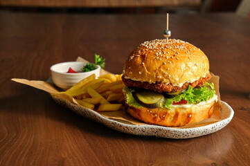 A delicious burger with a crispy patty, fries, and a drink on a wooden table.