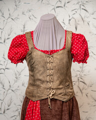 Festive lady outfit in vintage style (traditional leather waistcoat on lace in front, cowboy culture). Red blouse with lantern sleeves and scarf, brown cottage skirt. Outfit combined on the mannequin 