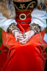Vintage crucifix (wooden cross, Symbol of Christian Faith) in female hands. Medieval lady costume, orange velvet dress, linen puff-sleeved shirt, furs and metal ornaments. Baptism of Slavic Spagans.