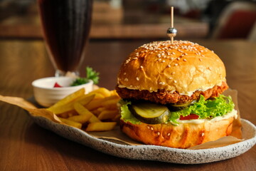 A delicious burger with a crispy patty, fries, and a drink on a wooden table.