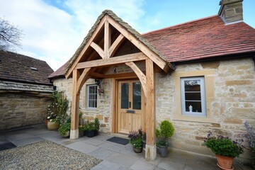 Charming stone cottage with wooden porch and colorful plants, located in a tranquil rural setting, creates a welcoming atmosphere for visitors in the countryside