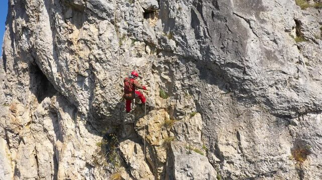 Aerial view of mountain rescuer rappelling on a rocky wall hanging on a rope