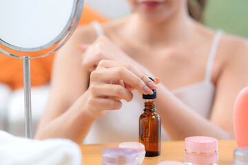 Fototapeta premium Closeup hands beautiful young woman applying lotion herb on hands looking mirror at home, beauty woman dropper serum for rejuvenation on hands, cosmetic and makeup for self care, skin care and health.