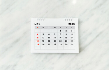 May 2025 desk calendar on white marble table on blurred office background.