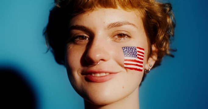 A young person stands still with eyes closed, showcasing a painted American flag on their face.