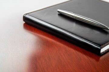 A black leather notebook rests on a mahogany desk with a silver pen.