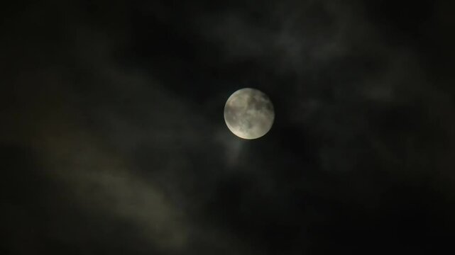 Full moon close up and cloudy sky on dark night. Clouds fly in front of the moon. Real shot of dramatic night sky