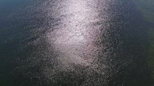 Hollywood Lake, County Monaghan, Ireland, April 2023. Drone high angle pullback above Crannog at center of lake as wind blows ripples with glistening light across surface