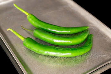 Green hot peppers with metal tray isolated on black background.