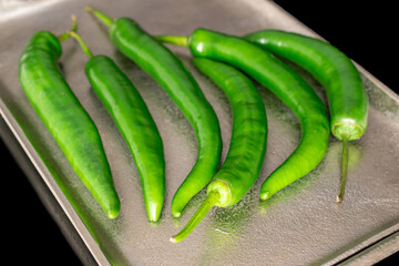 Green hot peppers with metal tray isolated on black background.