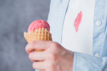 Unrecognizable person holding a waffle cone filled with strawberry ice cream while wearing a light blue button-up shirt. The backdrop is soft and neutral, creating a relaxed vibe.