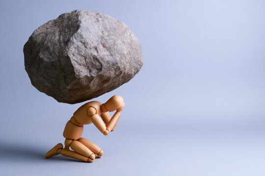 Conceptual wooden figures illustrate concepts of pressure and judgment as figure kneels under large rock symbolizing emotional burden