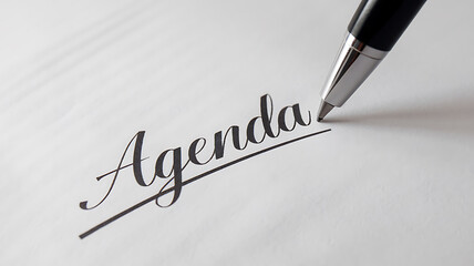 A pen rests near the word Agenda elegantly written on a crisp white surface suggesting planning and organization.
