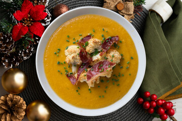 Pumpkin and cauliflower cream with crispy ham. Top view table with christmas decorations.