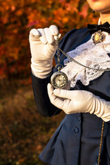 Vintage pocket watch in female hands. Victorian fashion attributes, abstract, close-up. Retro lady, vintage walking outfit in blue color. Glossy satin farbics for jacket and skirt, white gloves. 