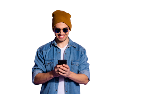 Photo of cheerful kind friendly blogger holding telephone with hands poting news in feed of social media smiling toothily wearing denim jacket isolated over purple vivid color background
