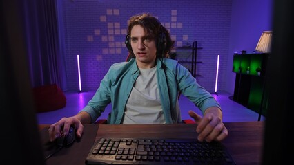 Young adult man spending time at home, man streamer gamer sits at desk with computer, streaming online and plays game, focused expression. Person pov. © kinomaster