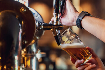 Close-up of a hand pouring beer from a tap into a glass, creating a frothy head. Set in a warm bar atmosphere. Ideal for themes of nightlife, hospitality, and drinks.