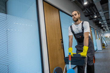 Young man in uniform walking in the office corridor and pushing the cart