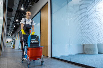 Smiling girl from the cleaning team pushing the cart and going to work place