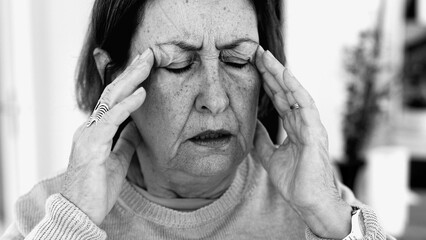 Elderly woman struggling with severe headache, massaging temples with visible concentration. Facial...
