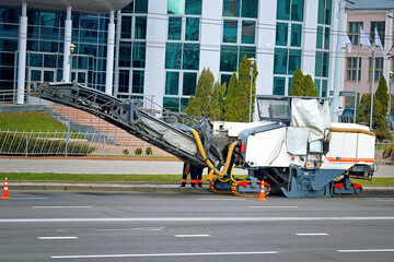 Road milling machine operating on an urban street for asphalt removal during road maintenance, surrounded by traffic cones and construction workers ensuring safety and progress, asphalt milling