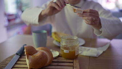 Grandmother carefully spreads butter on a slice of bread while sitting at a kitchen table. a simple and calm moment in her morning routine-SD 480p