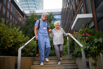 Caring healthcare worker helping elderly woman walk the stairs.